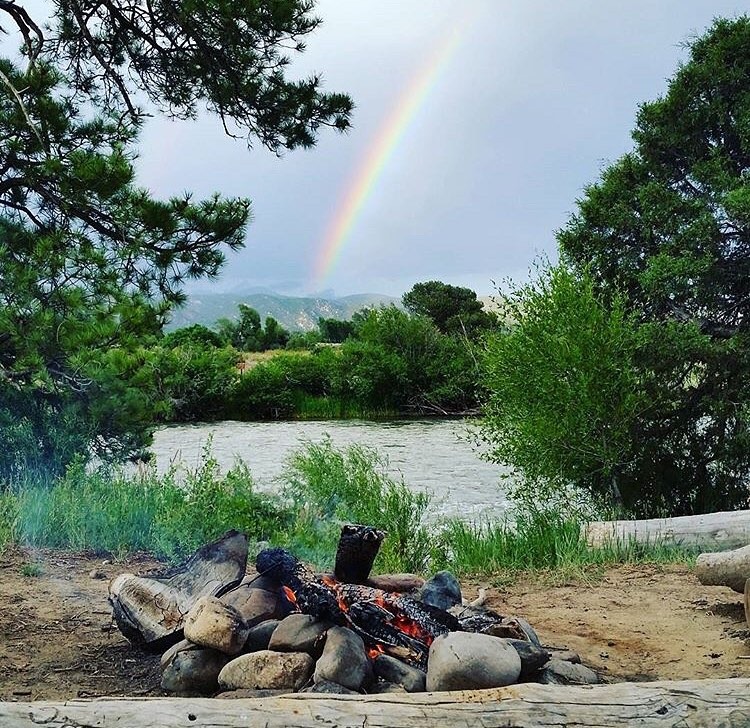 campfire near the river with a rainbow in the background