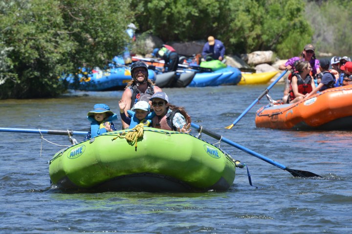 Group of people river rafting in green inflatable boat, with other rafts visible in background.