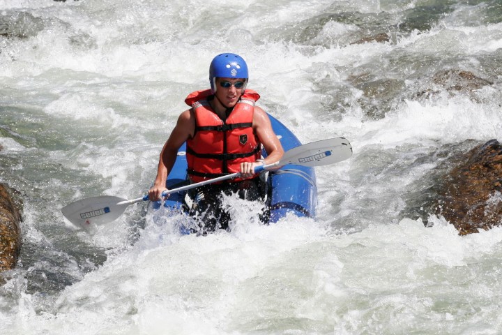 Person rafting in whitewater, wearing a helmet and life jacket.