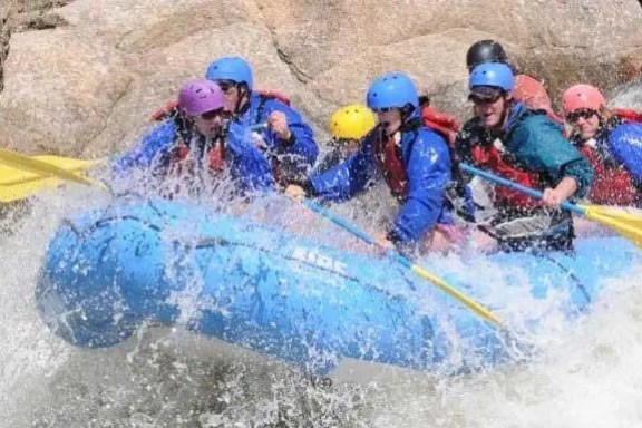 Group whitewater rafting in a river with safety gear and paddles.